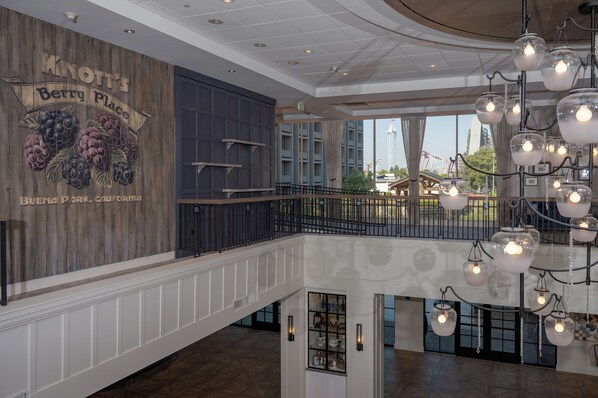 A spacious interior with a high ceiling, a wooden wall mural, a balcony with a railing, and hanging glass lamps.