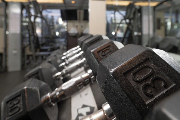 A close-up of a row of black dumbbells with visible weight markings, set against a blurred background of a gym interior. - Knott's Hotel (Buena Park)