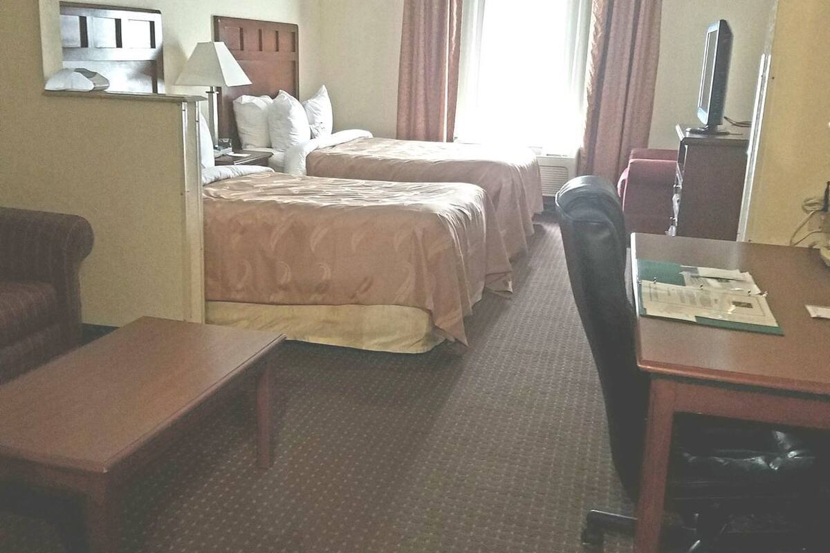 Quarto de hotel com duas camas, uma escrivaninha, uma cadeira, uma televisão e uma mesinha.