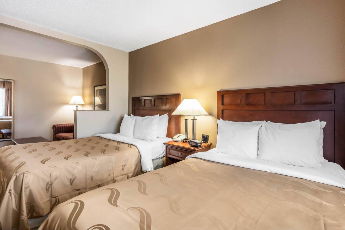 Quarto de hotel com duas camas, cada uma com cabeceira, mesas de cabeceira, luminárias e espelho.