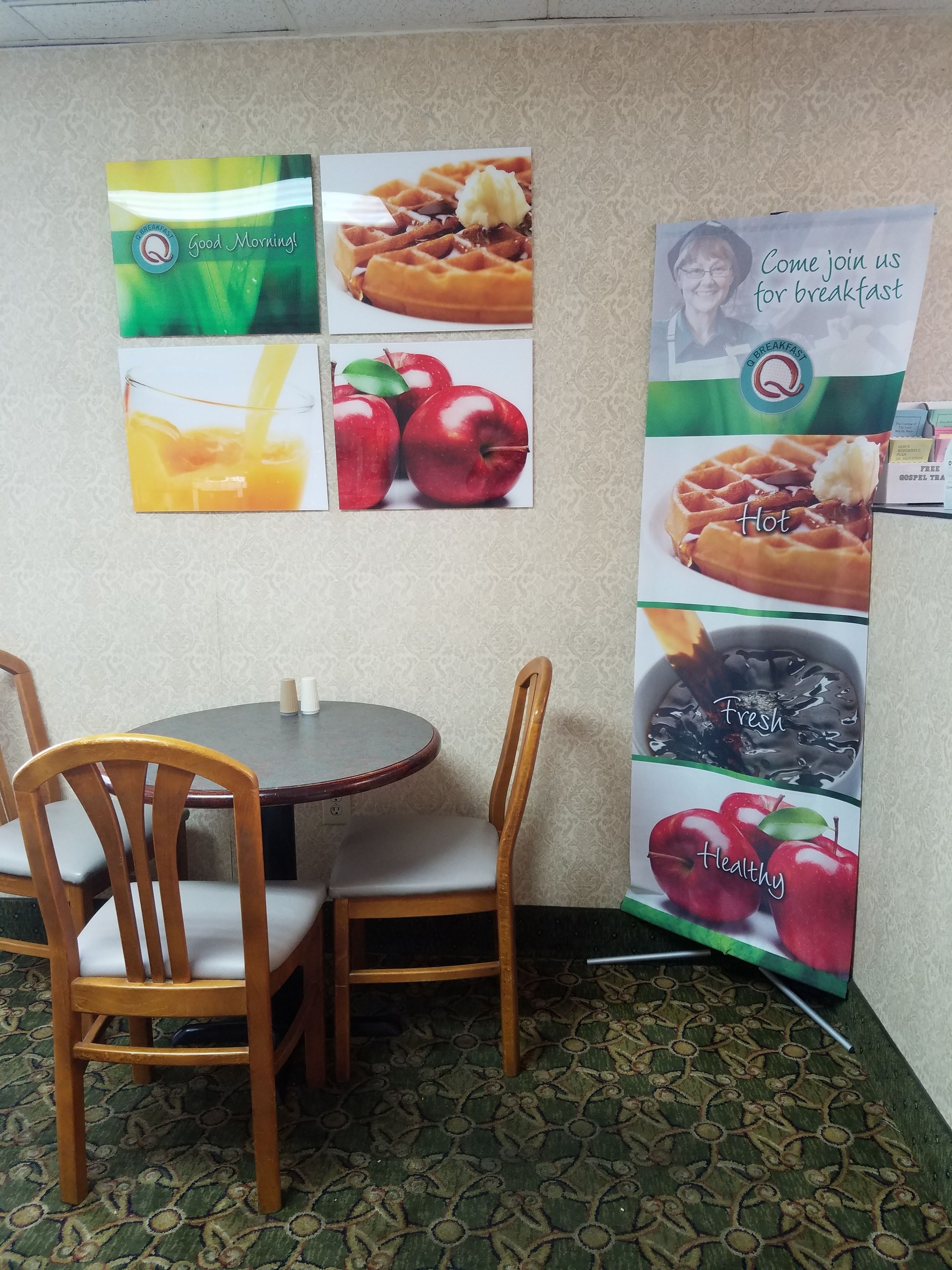 Comedor con una mesa redonda y dos sillas de madera. Hay carteles en la pared que anuncian opciones de desayuno.