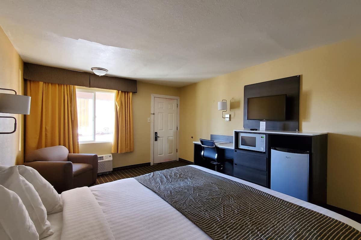 Ein Hotelzimmer mit einem Bett, einem Schreibtisch mit Computer, einem Fernseher und einer Mikrowelle.