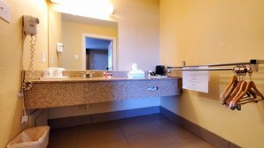 Een hotelbadkamer met een granieten aanrechtblad, een wastafel, een spiegel, een haardroger, een handdoekhouder en een prullenbak.
