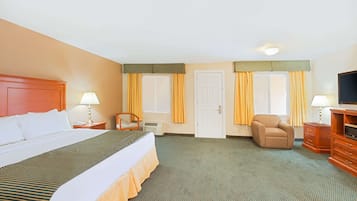 A hotel room with a bed, two chairs, a desk, a TV, and a door.