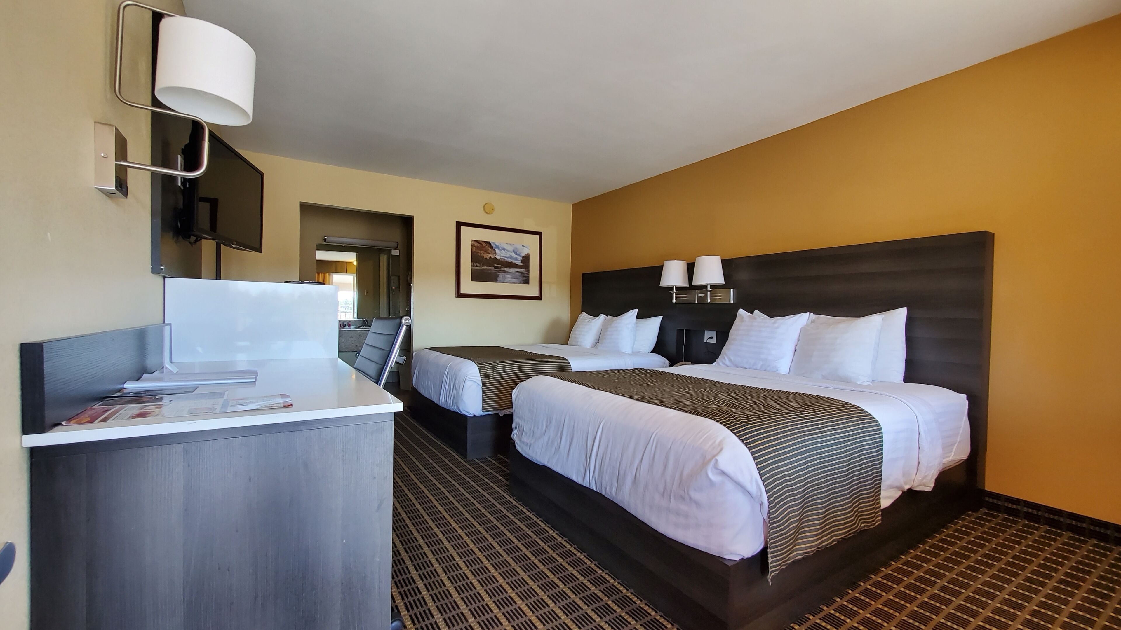 A hotel room with two beds, a desk, and a bathroom visible through an open door.