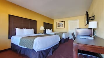 Habitación de hotel con dos camas, un escritorio con computadora, una lámpara y una puerta.