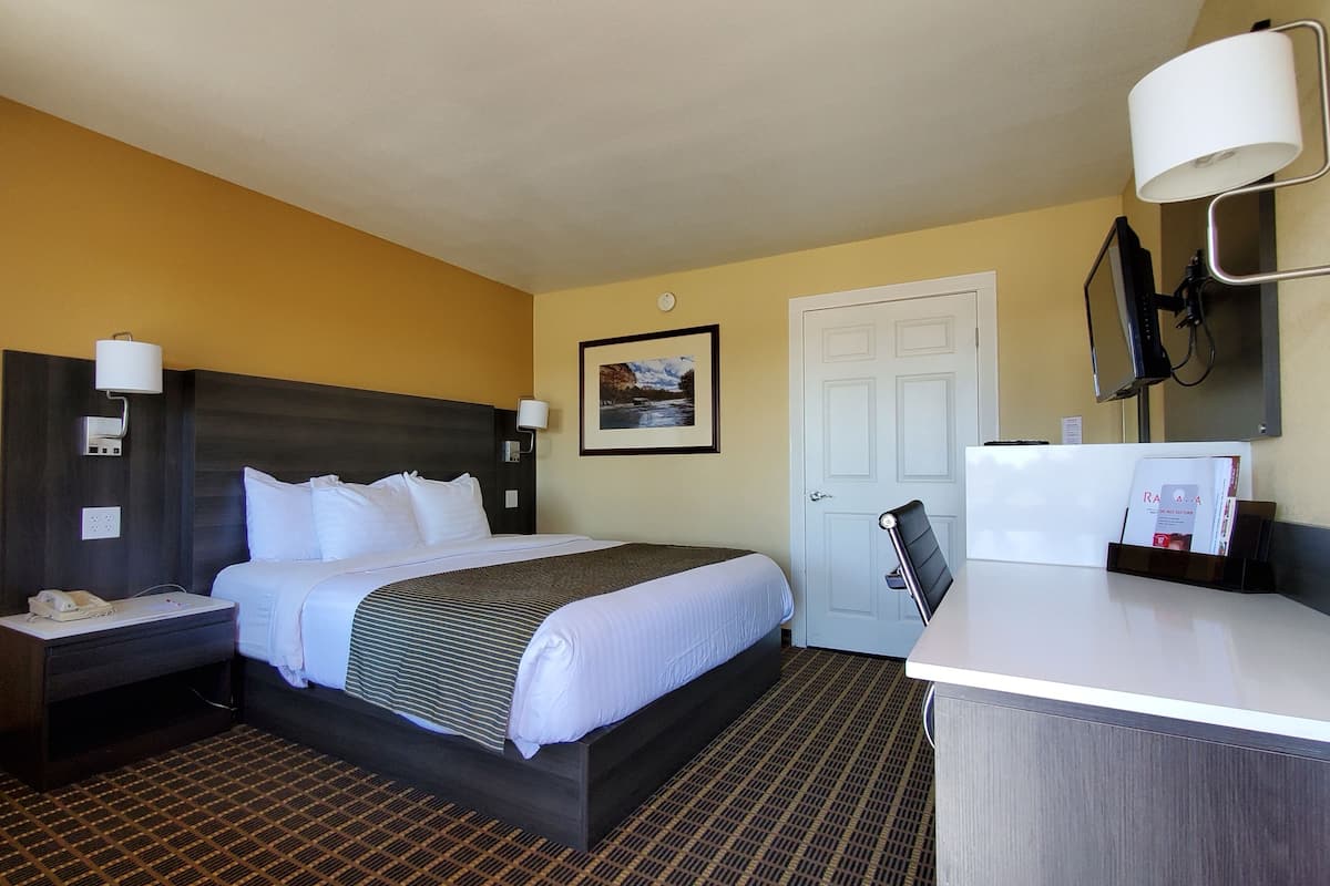 Ein Hotelzimmer mit Bett, Nachttischen, Schreibtisch, Stuhl, Lampe, Tür und einem gerahmten Bild an der Wand.