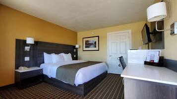 Habitación de hotel con cama, mesitas de noche, escritorio, silla, lámpara, puerta y un cuadro en la pared.