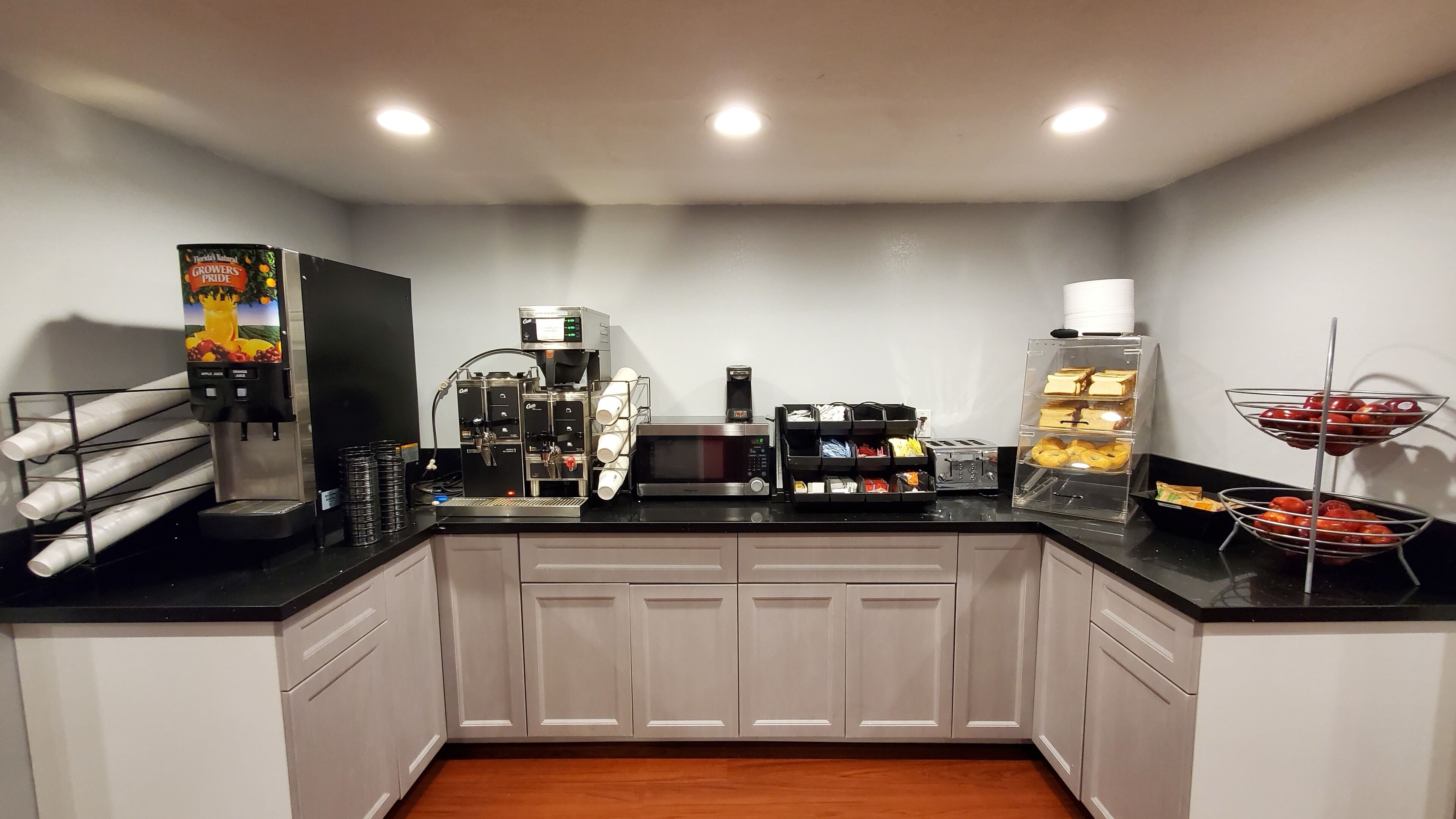 A kitchenette with a coffee machine, microwave, and a fruit display.
