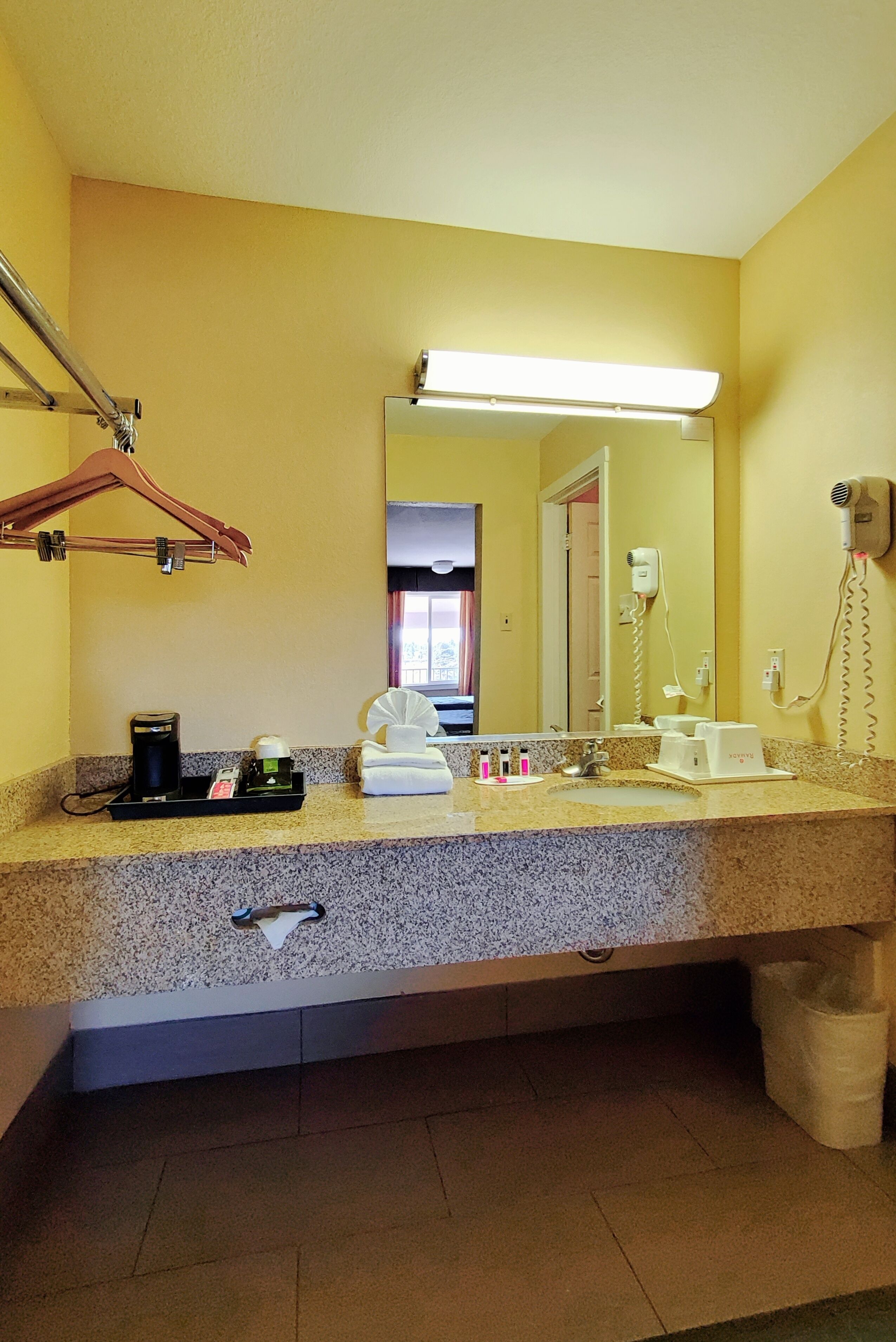 A hotel bathroom with a granite countertop, a mirror, a hairdryer, and a towel rack.