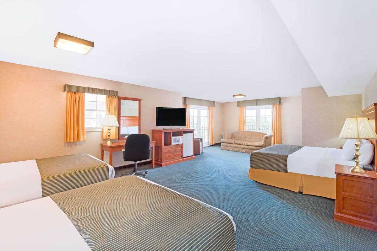 Ein Hotelzimmer mit zwei Betten, einem Schreibtisch, einem Fernseher, einem Sofa und einer Lampe.