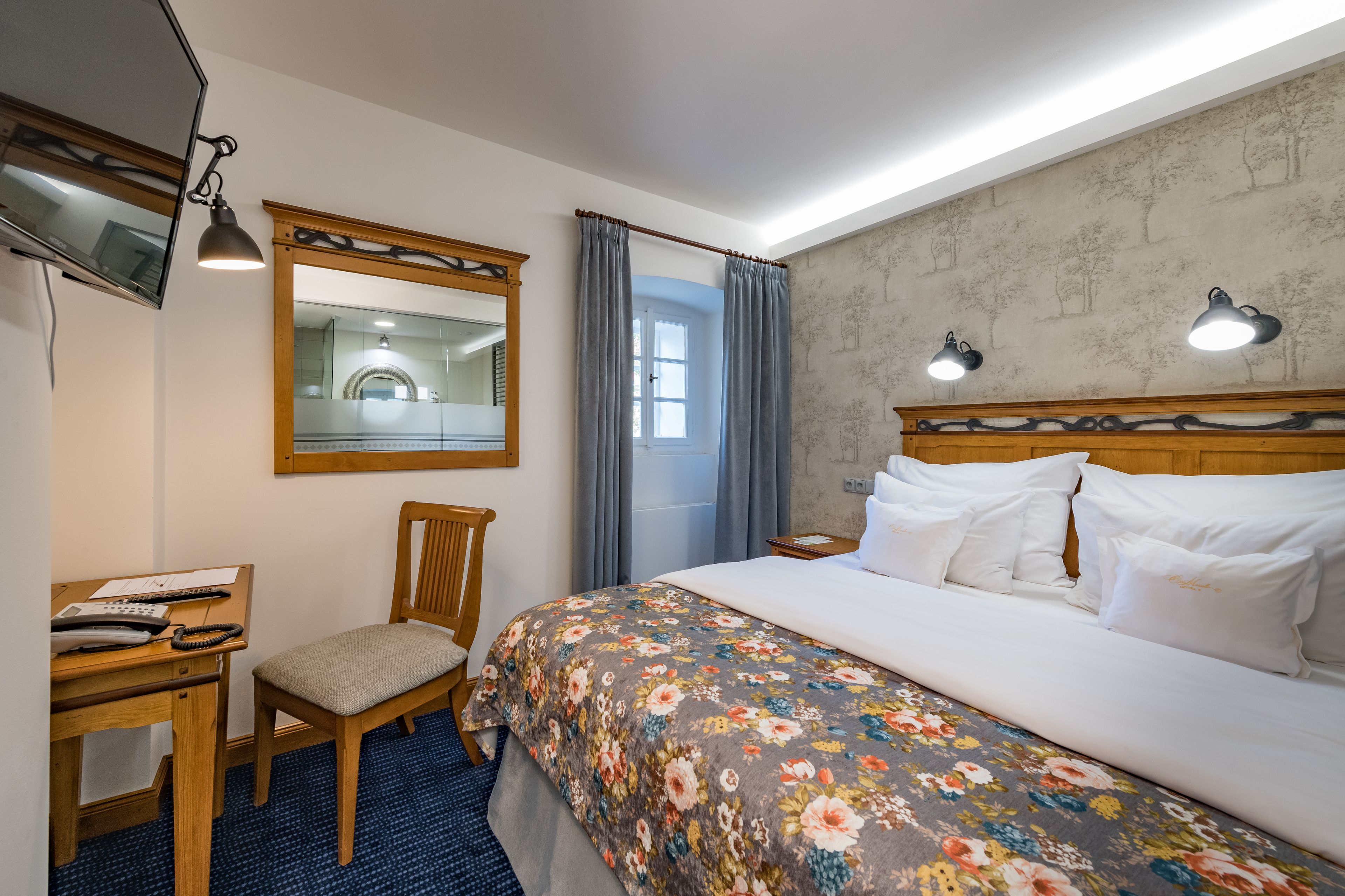 Habitación de hotel con cama, escritorio, silla, espejo y dos lámparas de noche.