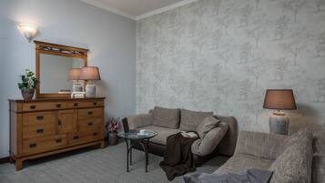 Ein Wohnzimmer mit einem Holzkontrollschrank, einem Sofa, einem kleinen Tisch mit Lampe und Wandpapier mit Muster.