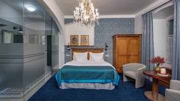 A hotel room with a large bed, a wooden wardrobe, a round table with a vase, and a chair.