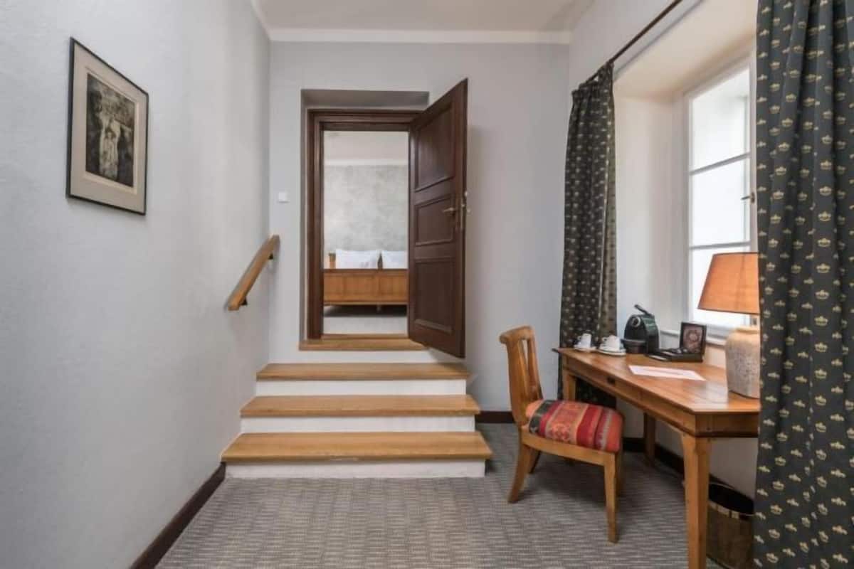 A staircase leading to a room, a wooden desk with a chair, a lamp, and a framed picture on the wall.