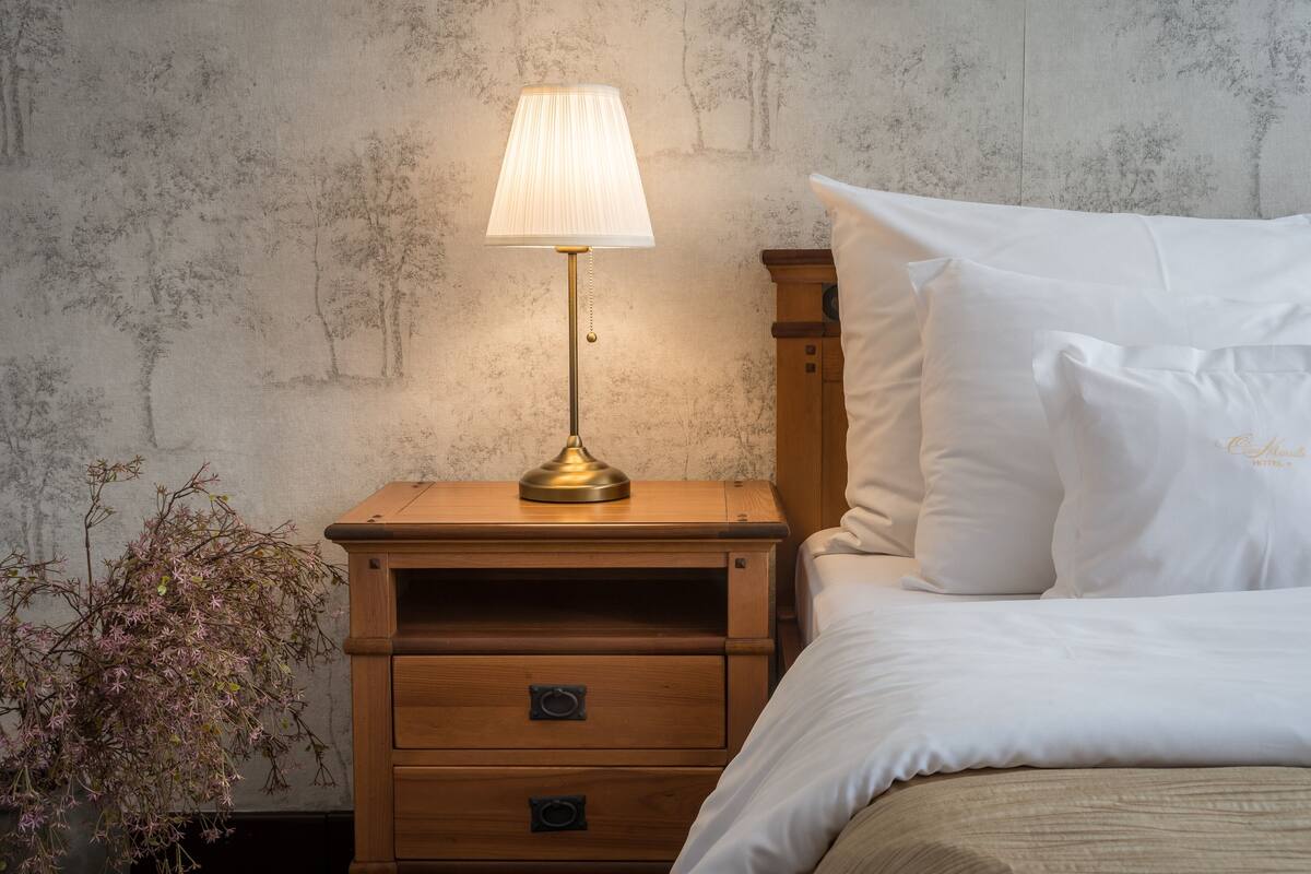 A neatly made bed with white linens, a bedside lamp, and a wooden nightstand with drawers.