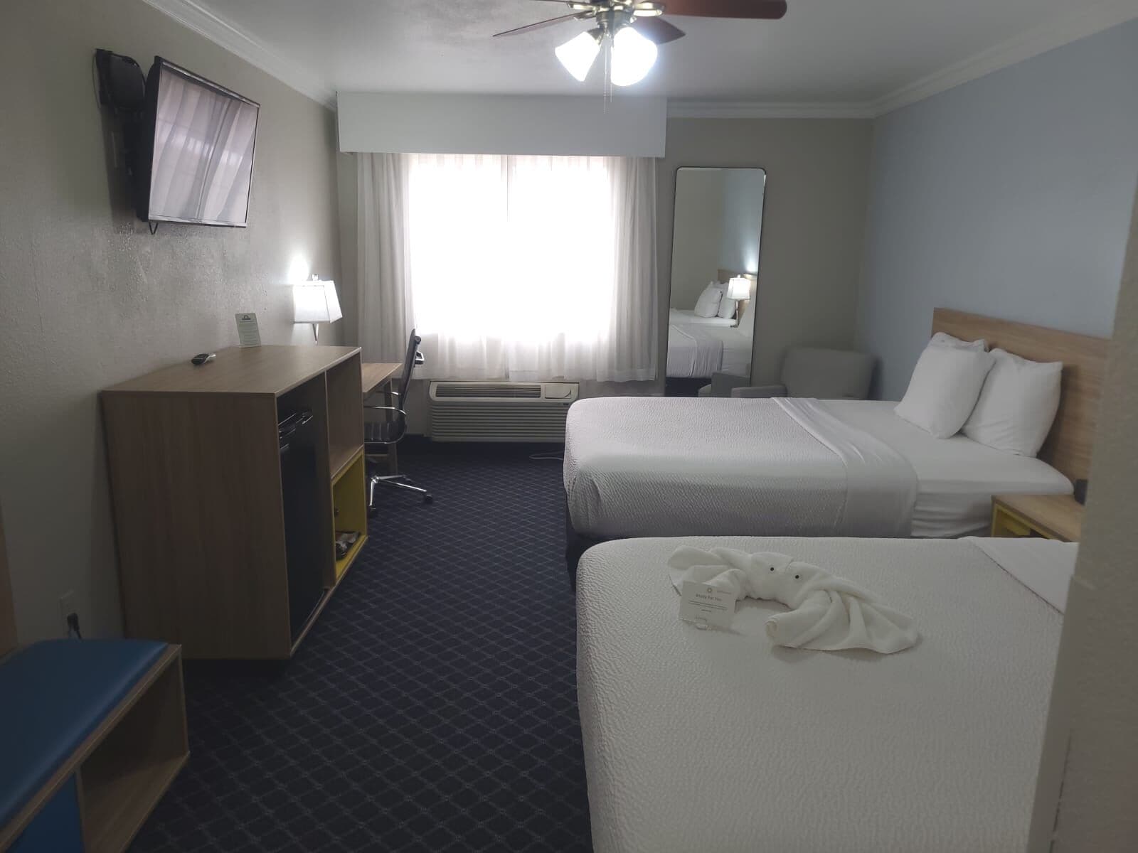 Una habitación de hotel con dos camas, un escritorio, una silla, un televisor y un ventilador de techo.