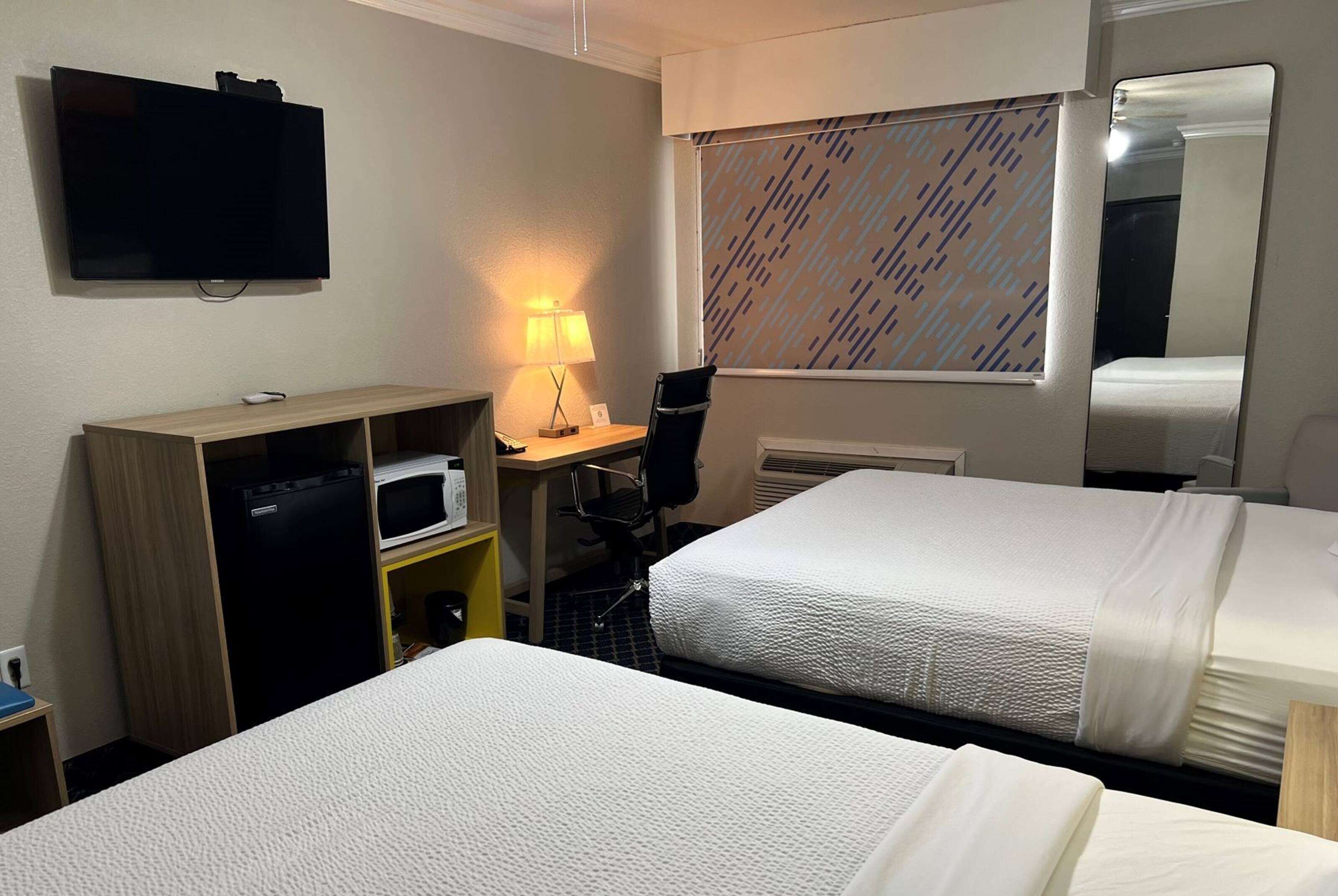Habitación de hotel con dos camas, un escritorio con computadora, un televisor, un microondas y una lámpara.