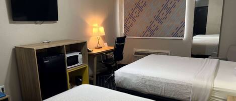 Habitación de hotel con dos camas, un escritorio con computadora, un televisor, un microondas y una lámpara.