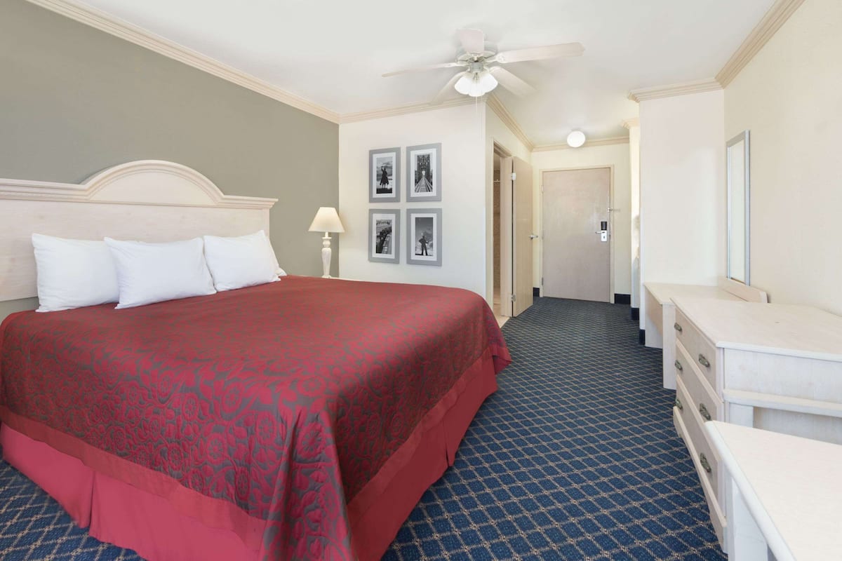 Habitación de hotel con una cama grande, un ventilador de techo, un aparador y una puerta que da a otra habitación.
