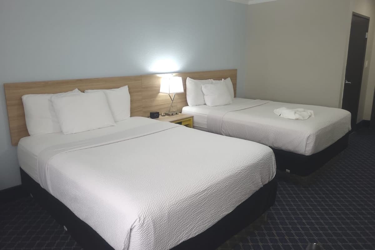 Una habitación de hotel con dos camas, una mesita de noche con lámpara y una puerta.