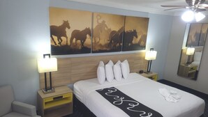 Een hotelkamer met een groot bed, twee nachtkastjes met lampen, een hoofdeinde, een spiegel aan de muur en een plafondventilator.
