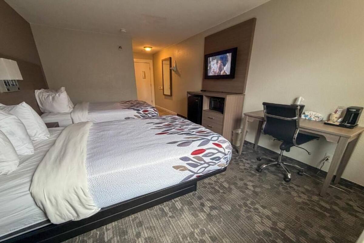 Una habitación de hotel con dos camas, un escritorio, una silla, un televisor y una kitchenette pequeña.