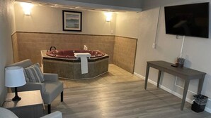 A modern bathroom with a bathtub, a sofa, a table, and a TV. - Whaler Inn and Suites (New Bedford)