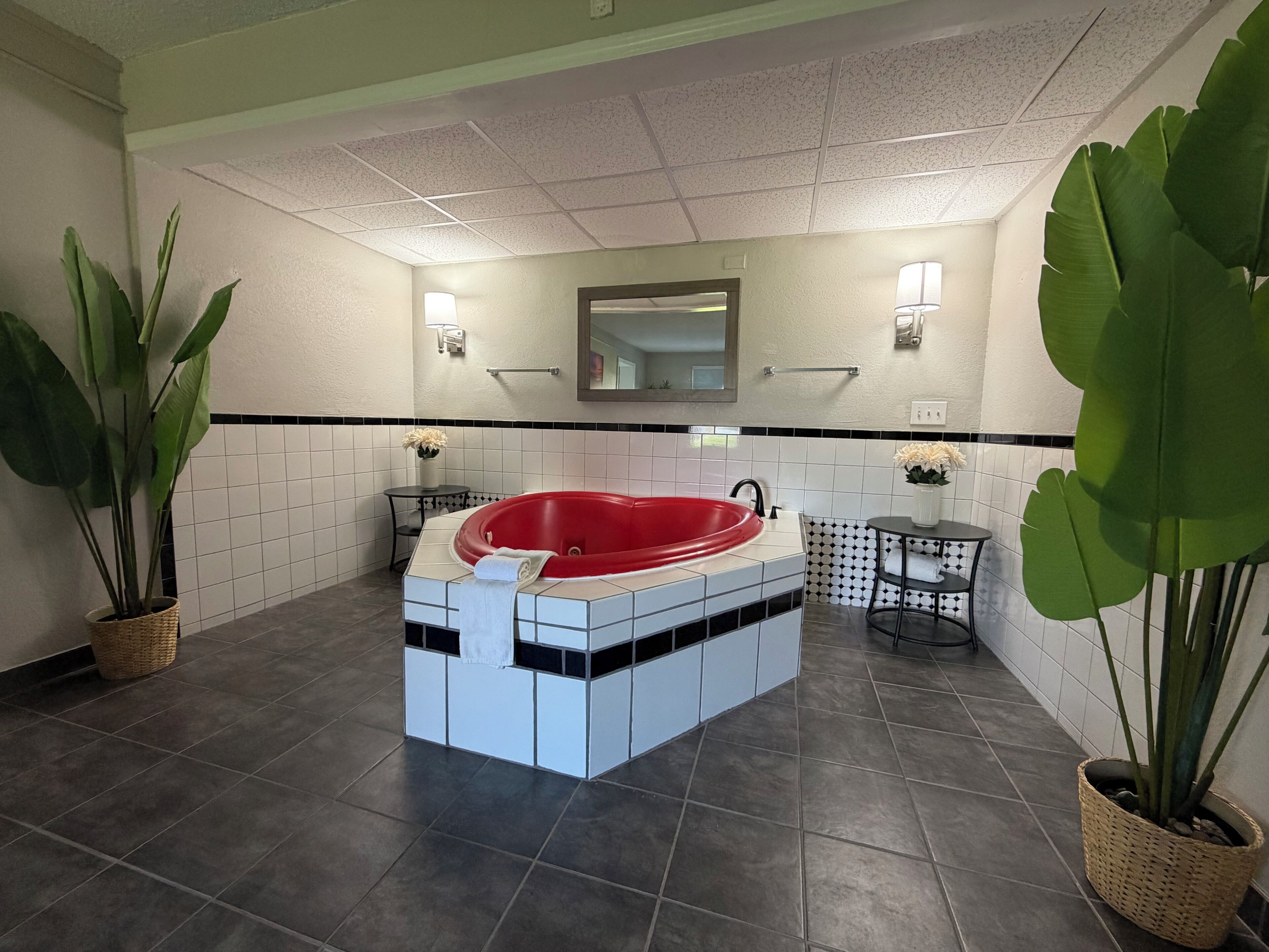 A bathroom with a red bathtub, white tiles, a mirror, and two potted plants.
