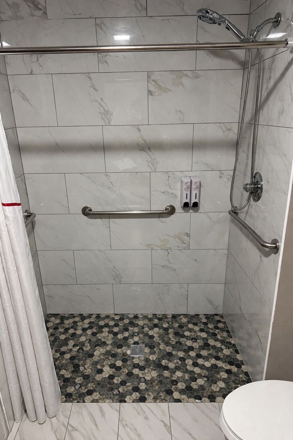 A bathroom with a shower, a handrail, and a toilet.