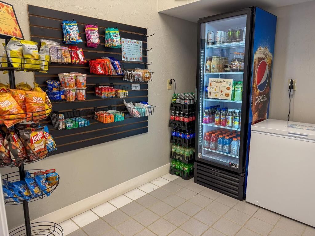A vending machine with snacks and beverages, a refrigerator with Pepsi, and a wall with snack bags.