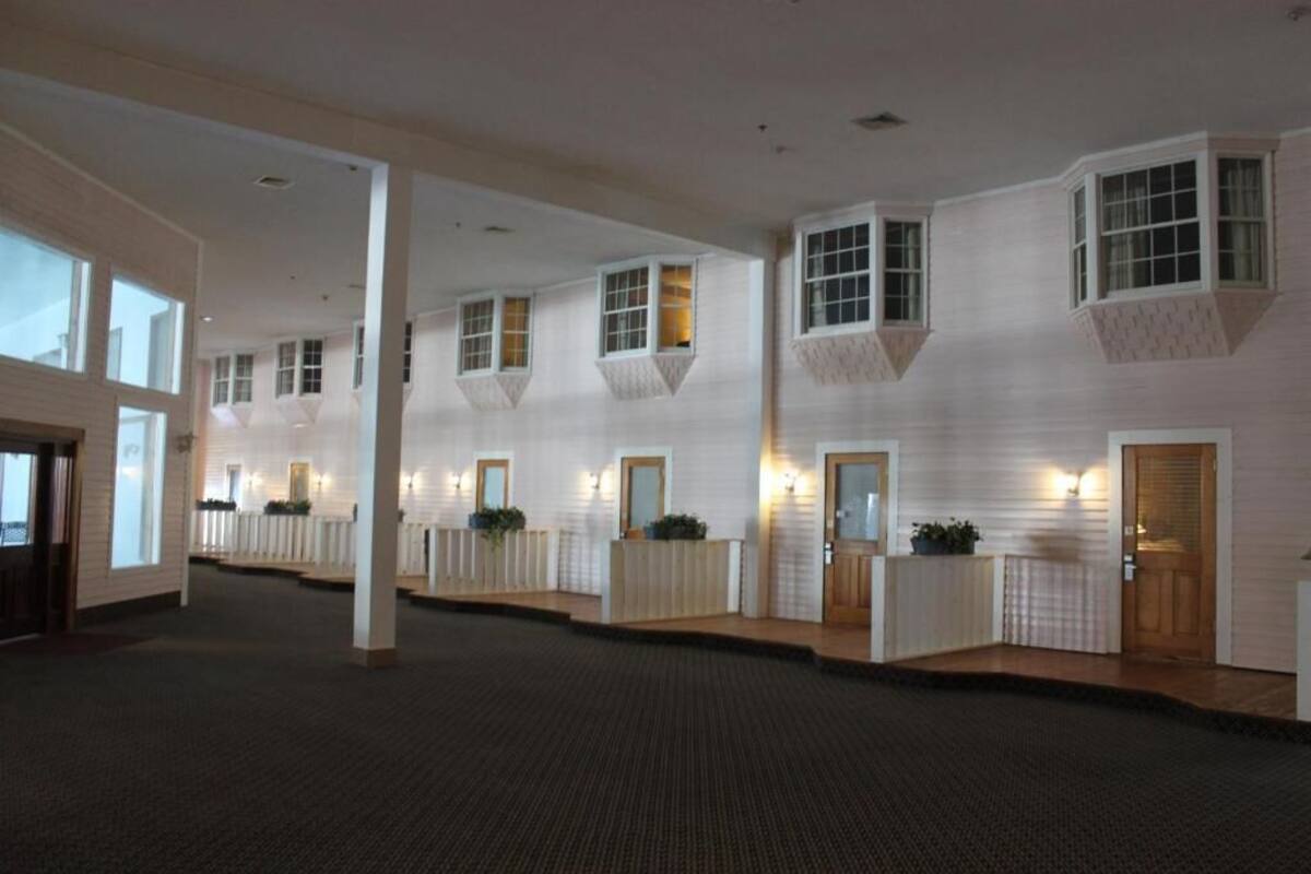 Interior de un hotel con un corredor central, varias habitaciones con ventanas y suelo alfombrado.