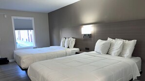 A hotel room with two beds, a window, a wall-mounted light, and a door. - Whaler Inn and Suites (New Bedford)