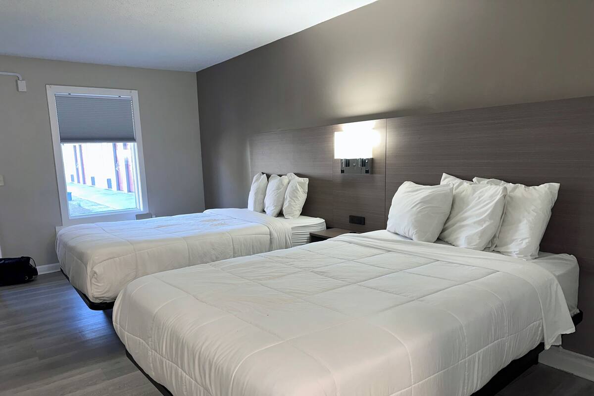 Habitación de hotel con dos camas, una ventana, una lámpara fijada a la pared y una puerta.