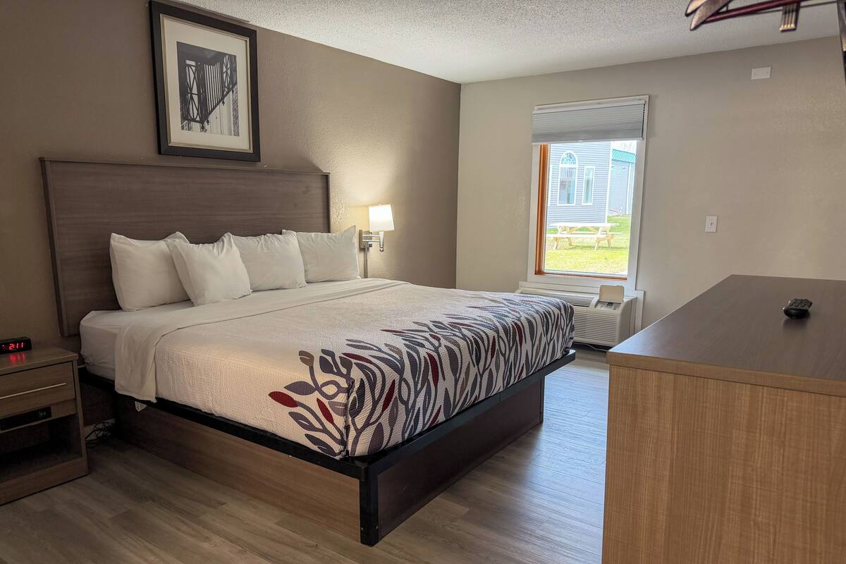 Un dormitorio con cama, mesita de noche, lámpara y vistas al exterior.