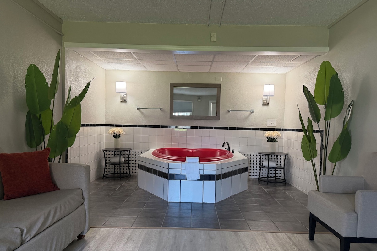 A spa room with a red jacuzzi, two side tables with plants, a sofa, and a tiled floor.
