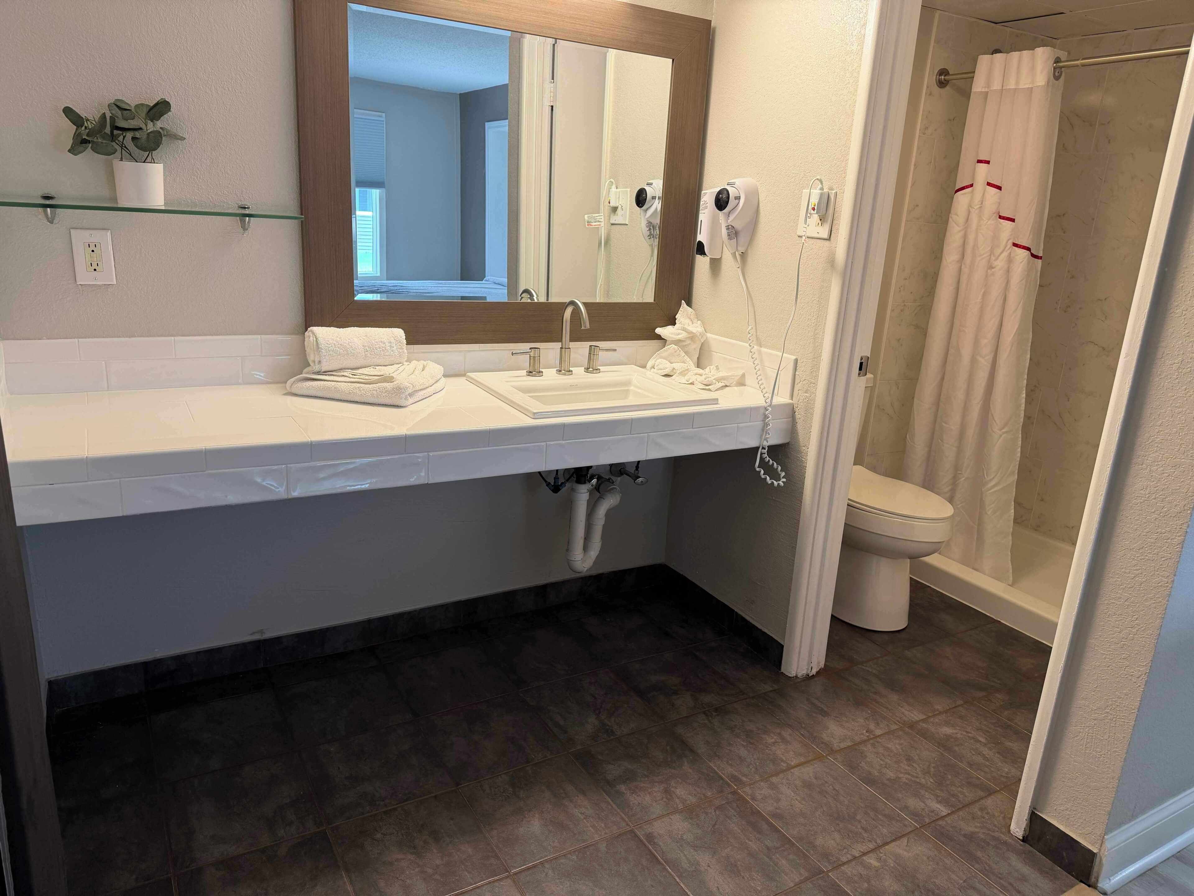 A bathroom with a white sink, mirror, and towel rack. There is a shower curtain and a toilet visible.