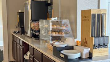 A breakfast buffet with a coffee machine, cereal dispenser, and a sign that says 'Good Morning Breakfast.'