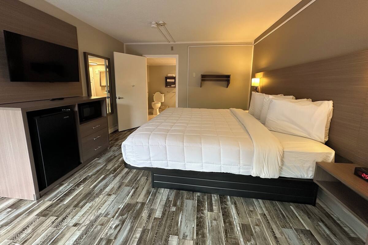 Habitación de hotel con cama, televisor, escritorio y baño visible a través de una puerta abierta.