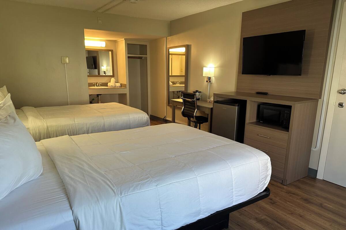 Habitación de hotel con dos camas, un escritorio, una silla, un televisor y un microondas.