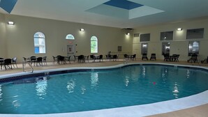An indoor swimming pool with clear blue water, surrounded by black lounge chairs and tables. - Whaler Inn and Suites (New Bedford)