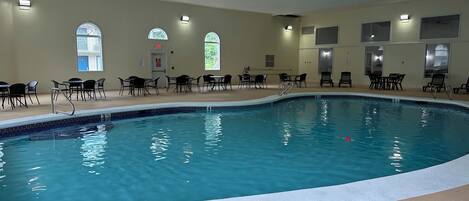 Una piscina interior con agua azul cristalina, rodeada de sillones y mesas negras.