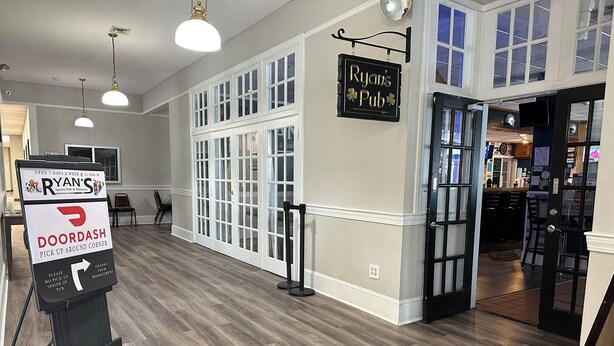A pub interior with a sign for Ryan's Pub, a pick-up area, and a bar visible through the open door. - Whaler Inn and Suites (New Bedford)