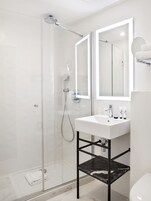 A modern bathroom with a glass-enclosed shower, a white sink with a black marble shelf, and a large mirror above the sink.