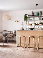 A modern kitchen with a bar area, wicker chairs, and a hanging light fixture.