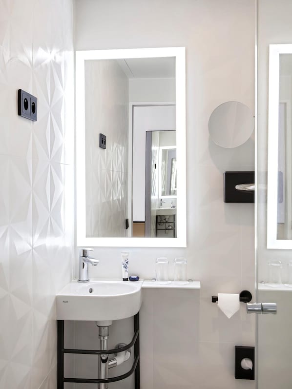 A modern bathroom with a white sink, a large mirror, and a glass shower enclosure. - Doisy Etoile - Orso Hotel (Paris)