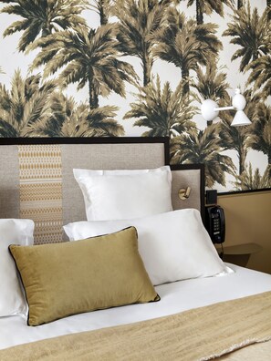 A hotel room with a bed, pillows, a patterned headboard, a nightstand with a phone, and a wall with palm tree wallpaper. - Doisy Etoile - Orso Hotel (Paris)