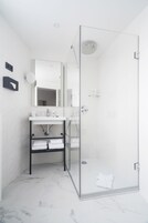 Ein modernes Badezimmer mit einer Duschkabine, einem weißen Waschbecken mit Spiegel darüber und einem Handtuchhalter mit gefalteten Handtüchern.