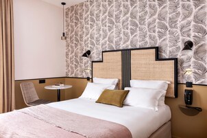 A hotel room with a bed, a small round table, a chair, and a wall-mounted phone.