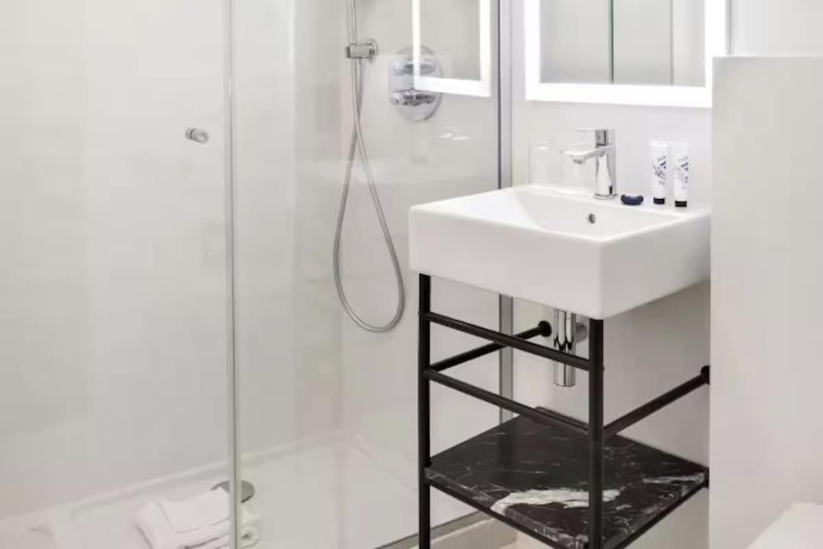 A modern bathroom with a glass-enclosed shower, a white sink, and a black marble shelf.